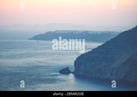 Lumière du coucher de soleil avec violet et rouge sur l'océan bleu avec vue floue sur Oia à Fira, Santorini, Grèce Banque D'Images