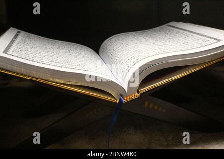 Livre du Coran sur un tapis marron, ouvert et isolé sur fond sombre Banque D'Images