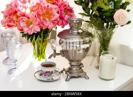Encore la vie avec le vieux samovar russe, une tasse de thé rustique, un bouquet de fleurs de pivoine, des verres et des bougies. Cérémonie de thé confortable dans un intérieur blanc. Banque D'Images