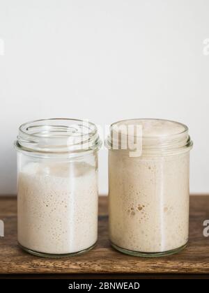 Deux pots en verre avec des démarreurs de levain de blé dans différents niveaux d'hydratation. Starter 100 % d'hydratation (droite) et Starter avec une hydratation plus élevée (gauche). Copier l'espace haut. Verticale. Banque D'Images