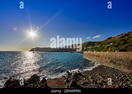 Image de la mer et du promontoire de bonne nuit Bay, derrière le mur du port au lever du soleil avec un ciel bleu clair, les îles du canal de Jersey Banque D'Images