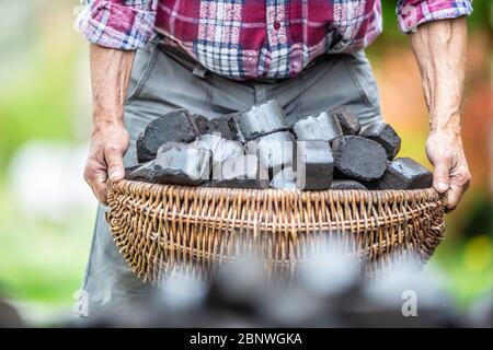 Détail des armes de l'homme ancien ramassant un panier rempli de briquettes de charbon. Banque D'Images