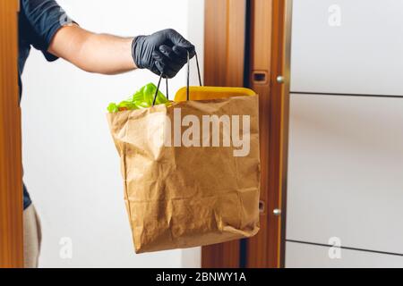 Livraison de magasin d'épicerie homme donnant sac en papier portant des gants noirs comme protection pour les précautions COVID-19 coronavirus. Banque D'Images