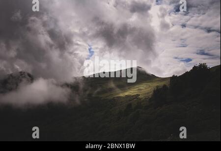 Belle vue d'une immense montagne couverte de nuages de pluie intense avec lumière du soleil piquant à travers un patch sur le côté et tombant sur la montagne Banque D'Images