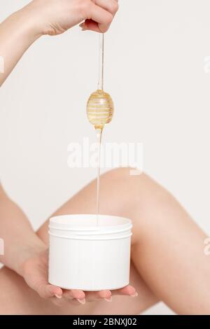 Femme tenant le bâton de miel tout en coulant la cire liquide dans le récipient sur fond blanc. Banque D'Images