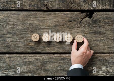 Image conceptuelle de qualité et de luxe - main de sexe masculin plaçant un cercle en bois coupé en forme de coeur sur lui dans une rangée de cinq. Sur fond de bois rustique. Banque D'Images