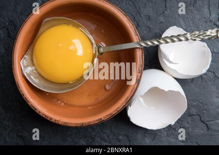 Jaune de poulet provenant d'œufs biologiques cassés dans une plaque brune sur fond de béton noir. Photographie alimentaire Banque D'Images