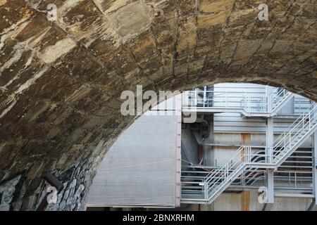 arche en cubes de pierre donnant vue sur une partie arrière d'un bâtiment industriel avec tuyaux et escalier métallique Banque D'Images