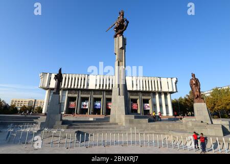 Orchestre philharmonique national kirghize de style Brutaliste à Bichkek, au Kirghizistan, nommé en l'honneur du musicien Toktogul Satylganov. Fleurs rouges et statue de Manas. Banque D'Images