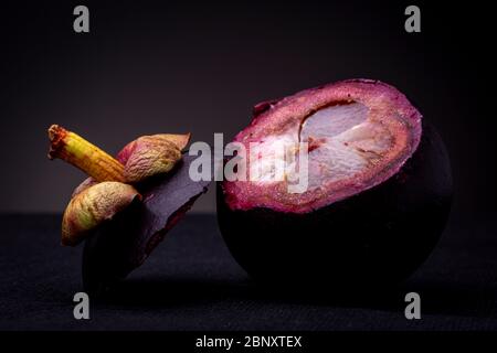 Tige colorée et dessus reposant en plus du fruit Mangosteen exotique rouge-violacé montrant sa chair blanche interne et son épais zeste rouge spongieux. Banque D'Images