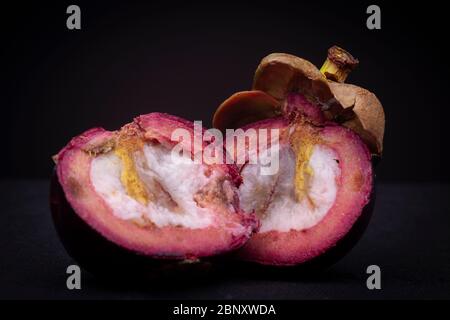 Deux moitiés d'un fruit de mangoustan exotique rouge-violacé montrant la pulpe blanche intérieure et la couche épaisse de peeling rouge avec le dessus encore. Banque D'Images