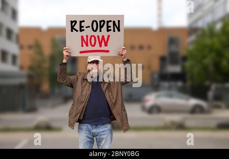 Le manifestant avec chapeau et lunettes de soleil démontrera contre les commandes de séjour à la maison en raison de la pandémie COVID-19 portant l'affiche indiquant réouverture. Bâtiments flous Banque D'Images