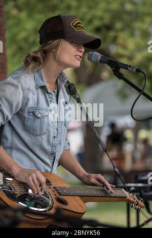 Jolie femme blonde, jouant de la guitare acoustique sur les genoux et chantant au concert en plein air. Porter un capuchon de boule Banque D'Images