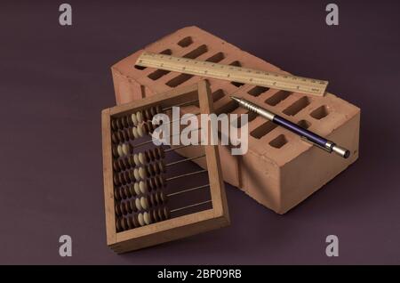 Expérience comptable dans le secteur du bâtiment. Fond créatif avec des objets thématiques dans des couleurs calmes. abacus en bois, brique rouge, règle et stylo. Sélectif Banque D'Images