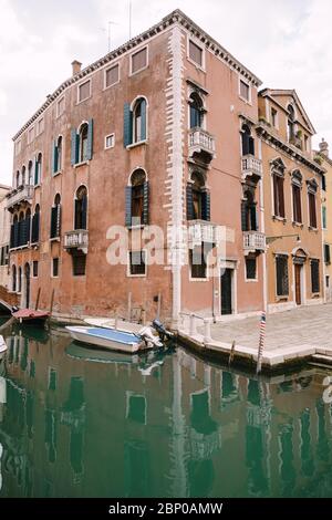 Vue en grand angle d'une maison de trois étages, couleur pêche, près d'un petit canal vénitien étroit. Un bateau à moteur amarré près des murs d'une maison debout Banque D'Images
