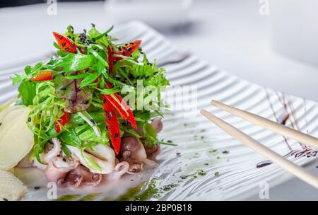 Salade gastronomique avec poulpes, arugula et légumes sur une assiette blanche et baguettes pour les aliments. Banque D'Images