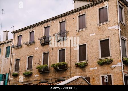 Gros plan de la façade d'un bâtiment, dans les rues de Venise, Italie. Un bâtiment de trois étages en briques avec des volets bruns fermés, pots avec vert luxuriant Banque D'Images