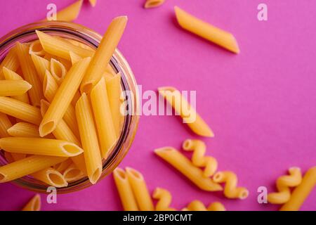 Un pot en verre avec des pâtes de blé doré non cuites sur fond rose minimal, vue de dessus macro Banque D'Images