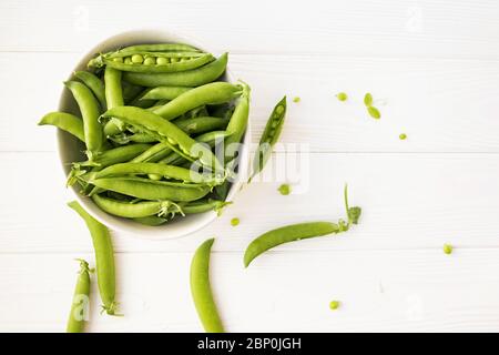 Petits pois verts frais dans un bol en céramique sur une table blanche, vue du dessus. Banque D'Images