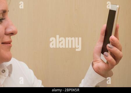 Femme parle par chat vidéo mobile. Une femme d'âge moyen blanche tient le téléphone devant son visage et passe un appel vidéo. Chemise d'affaires blanche habillée. Banque D'Images