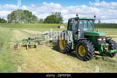 tracteur dans le champ avec faneuse d'herbe pendant la récolte du foin aux pays-bas sous ciel bleu Banque D'Images