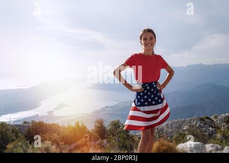 Enfant adolescent gir sur le sommet de la montagne avec un drapeau américain sur les hanches. Heure du coucher du soleil Banque D'Images