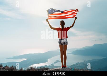 Une fille agite le drapeau américain sur le sommet de la montagne, sur fond de ciel Banque D'Images