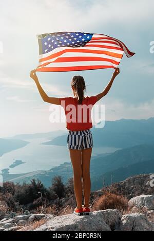 Une fille agite le drapeau américain sur le sommet de la montagne, sur fond de ciel Banque D'Images