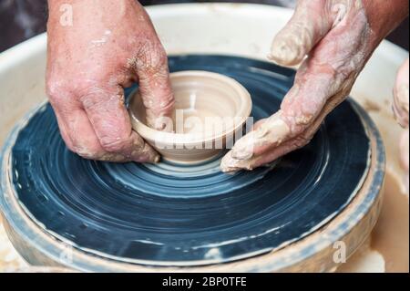 Le potter qui fait des plats de poterie sur tour de potier. Le sculpteur à l'atelier d'argile rend libre. Les mains de potter. Banque D'Images