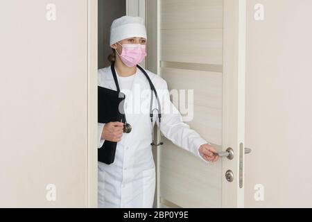 Le médecin portant un masque médical avec stéthoscope ouvre une porte qui entre dans la pièce Banque D'Images