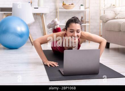 Jeune femme sportive s'exerçant à la maison, faisant des push-up près d'un ordinateur portable, regardant l'entraînement en ligne tutoriel Banque D'Images