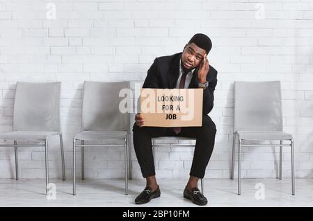 Afro-américain gars à LA RECHERCHE D'UN EMPLOI affiche assis dans le foyer de la compagnie, en attente de l'entretien de travail. Espace libre Banque D'Images