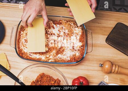 Mains d'homme faisant des couches de lasagnes dans un plateau en verre, Banque D'Images