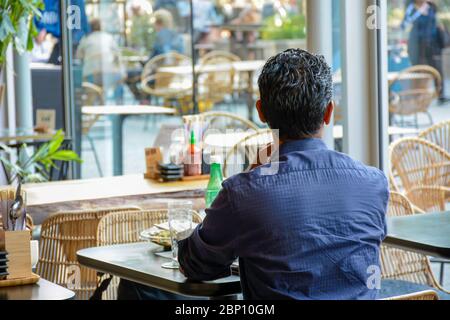 L'homme de derrière s'assoit seul dans un café-restaurant moderne et regarde dehors. Il attend son compagnon pour revenir. Il n'y a personne d'autre autour de lui. Banque D'Images