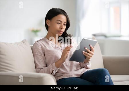 Une femme africaine s'assoit sur un canapé en utilisant un gadget de tablette Banque D'Images