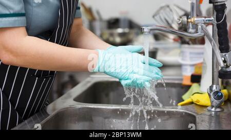 Femme en gants bleus se lavant les mains à fond sous l'eau Banque D'Images