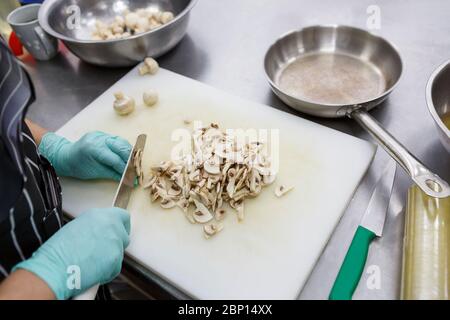 Mains en gants coupant des champignons à bord, préparant des aliments sains Banque D'Images