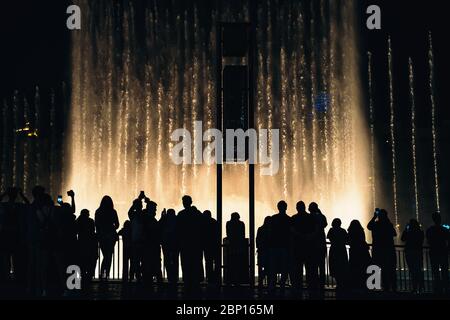 Fontaine de Dubaï avec silhouettes de personnes en premier plan la nuit. Lieu touristique populaire, eau. Banque D'Images
