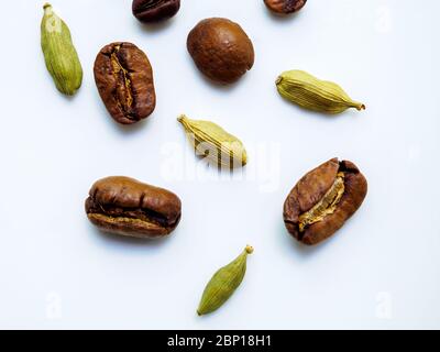 Pose à plat. Les grains de café et de cardamome sont éparpillés sur une surface blanche brillante. Faible profondeur de champ et arrière-plan très flou. Copier l'espace. Banque D'Images