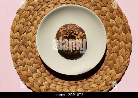 Un donat au chocolat décoré de boucles au caramel sur le dessus de la plaque blanche sur le tapis brun clair, fait à la main de jacinthe d'eau et clair Banque D'Images