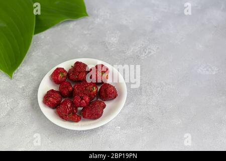 Produit naturel laid de fraises sur un plat blanc, rouge mûr et formes étranges sur fond gris. Une cuisine à la mode et insupportable. Étrange drôle imparfait Banque D'Images