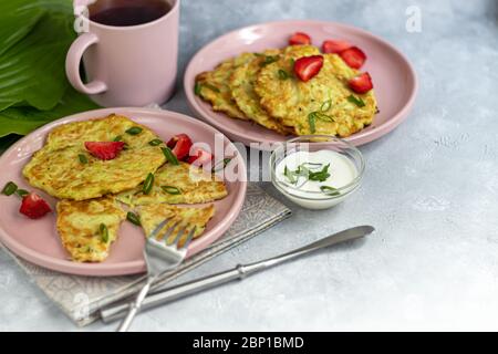 Beignets de courgettes, beignets de courgettes végétariennes, servis avec des herbes fraîches et de la crème aigre. Garni de fraises et d'oignons verts. Sur un gris clair Banque D'Images