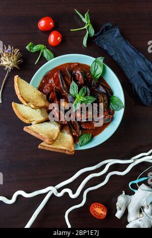 Moules à la sauce tomate au basilic et tranches de pain dans une assiette bleue sur une assiette en bois servies avec des légumes Banque D'Images