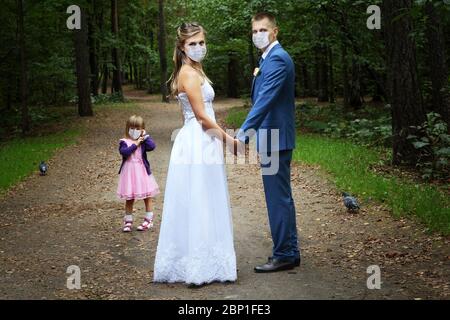 La mariée et le marié marchent dans le parc avec une petite fille pendant la pandémie d'infection à coronavirus Covid-19 et l'isolement à domicile, tous portent un médecin Banque D'Images