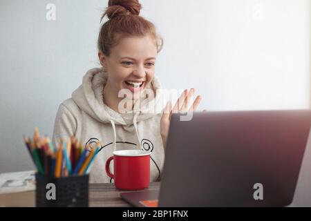 Jeune femme caucasienne avec un ordinateur portable à la maison, faisant un appel vidéo, parlant et souriant. Restez en contact avec le concept familial Banque D'Images