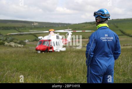 Un membre de l'équipe de recherche et de sauvetage de HM Coastguard regarde comme un hélicoptère AW189 AgustaWestland depuis les terres de HM Coastguard sur le côté de la falaise près d'Overcombe à Dorset, au cours d'un exercice d'entraînement. Banque D'Images