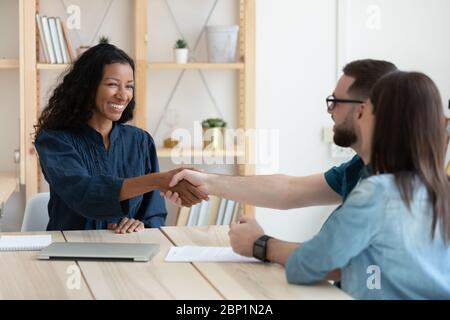 Agent immobilier qui se fait des mains avec un jeune couple heureux. Banque D'Images