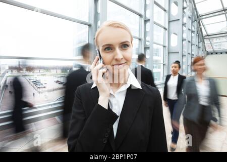 Femme d'affaires parlant au téléphone debout dans une foule de personnes marchant Banque D'Images