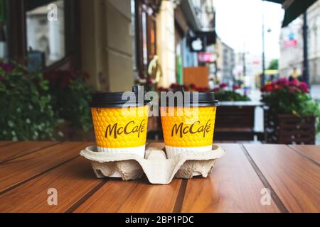 Lviv, Ukraine - 17 mai 2020 : restaurant McDonalds dans le centre-ville, deux tasses de café jaunes de McCafe sur une table en bois avec fond de ville. Réf Banque D'Images