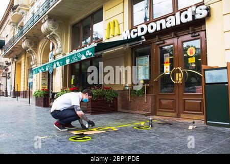 Lviv, Ukraine - 17 mai 2020 : homme marquant l'espace de rue devant le restaurant McDonalds avec panneau GARDER LA DISTANCE et les lignes d'avertissement. Santé, social Banque D'Images